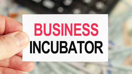 A man holds a piece of paper with the text: BUSINESS INCUBATOR. Business and finance concept.