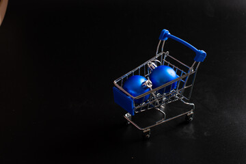 Two blue Christmas balls in a shopping cart on a black background. Copy space. Happy new year and christmas concept