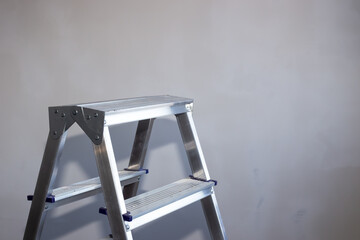an aluminum stepladder stands against a gray wall. Repair and improvement of housing. Copy space to the right