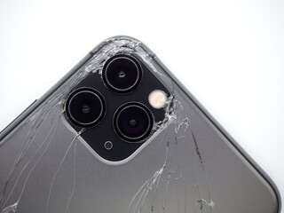 The back of the space grey modern smartphone has broken glass on white background. Modern smartphone with damaged back glass.