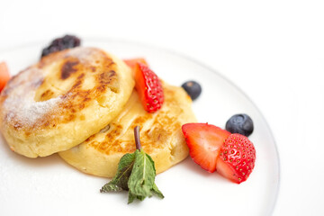 Two appetizing syrniki with fresh blueberries and strawberry slices white plate