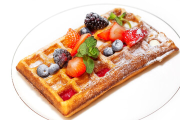 Fried waffle sprinkled with powdered sugar with pieces fresh fruits and berries