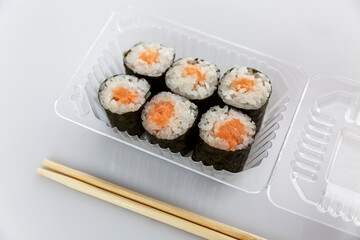 Appetizing fish rolls in a plastic container. Traditional Asian food. Grey background.