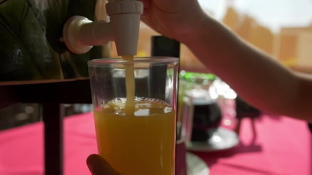 Female hands serving a glass of orange juice above a red table