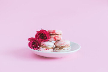 Tasty french macaroons with pink roses in a white cup. Heart-shaped macaron. Pink pastel background.