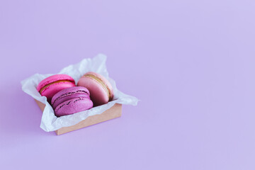 Tasty french macaroons in a box on a violet pastel background.
