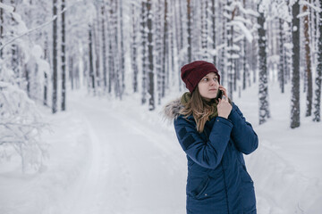 Fototapeta na wymiar Beautiful girl calls a taxi in the winter forest