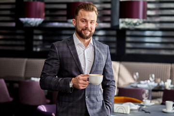 Fototapeta premium businessman stand waiting for partner, holding cup of coffee. working day, meeting in restaurant, smiling