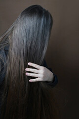 young long haired brunette unraveling combing her hair with a wooden brush with natural bristles on dark brown background, concept of hygiene, hair care