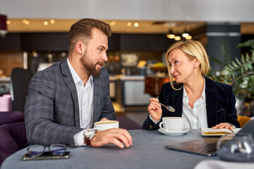 middle-aged man and woman discussing projects using laptop, at business meeting, in formal wear