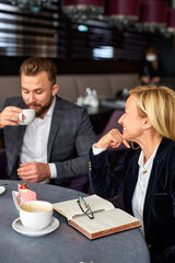 two business partners chatting over a cup of coffee, thinking and talking, discussing business ideas and projects, in restaurant. focus on smiling woman