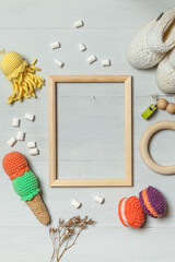 Wooden frame on a gray background and toys for babies. Knitted sweets, wooden rattle and knitted...
