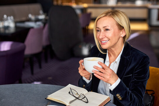 business woman sitting in restaurant with notebook, drinking cup of coffee, smiling, enjoying free time, smiling