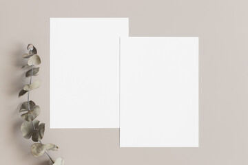 Two white invitation cards mockup with an eucalyptus decoration on the beige table. 5x7 ratio, similar to A6, A5.