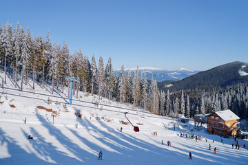 Snowy mountains and ski lifts. Skiers and snowboarders skiing downhill to village.