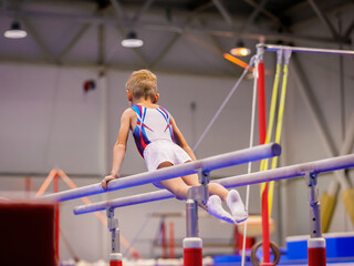 A little boy in sportswear performs an exercise on the uneven bars. Rhythmic gymnastics, training in the hall.