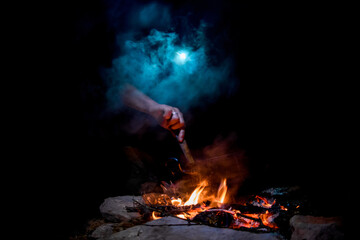 night view of bonfire with saucepan and man's hand stirring dish in it