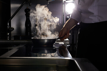 Cropped chef at kitchen restaurant. Cook in white uniform professionally preparing meal on stove, fries a dish for guests. close-up photo, side view