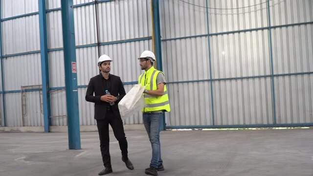 Executive business man or owner walking with foreman holding blueprint checking plans in construction site warehouse building indoors . architect discussion with engineer