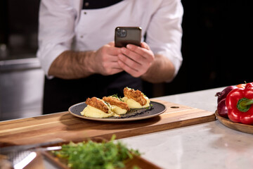 Cropped Chef Cook Take photo of Dish prepared by him, using smartphone. tasty yummy meal on plate is going to be served for restaurant guests