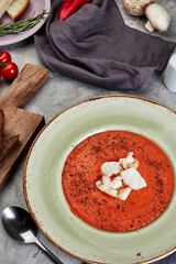 tomato soup with melted cheese in a plate on gray concrete background