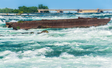 The Niagara Scow sits in the raging water of the Niagara River close to the edge of the Horseshoe Falls in Niagara Falls Canada.
