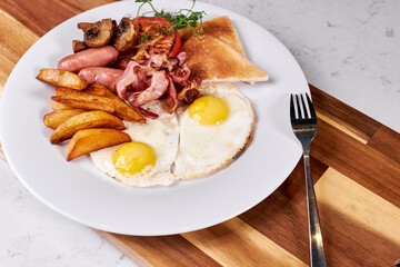 Breakfast plate with fried eggs, fries, fried bacon, crispbread, sausages, tomato in restaurant. Beautifully decorated and served dish, meal cooked by professionals