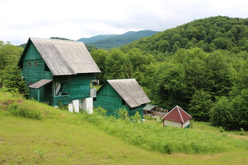 Fototapeta na wymiar Village green landscape. Cottage at the beautiful mountains background