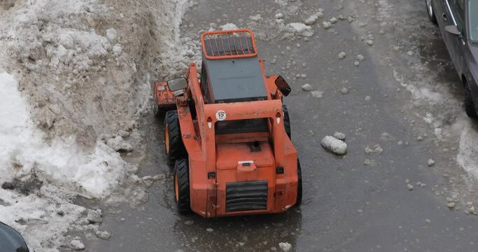 Winter snow removal from sidewalks. A mini tractor shovels snow onto the side of the road. View from above.