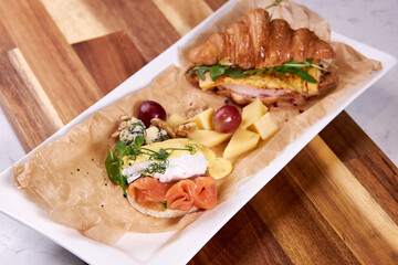 Delicious food flat lay, croissant, cheese, grapes and vegetables on wooden board close-up. Beautifully served meal for guests in restaurant