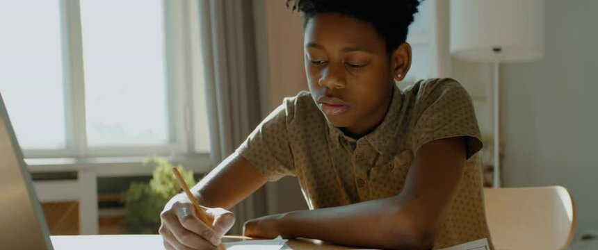 African American Black kid boy doing his homework at home. Distance learning from home during isolation. Shot with 2x anamorphic lens