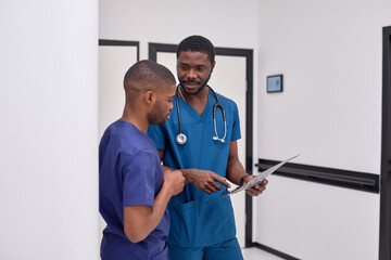 Two african american male colleagues doctors working together, discussing and looking at clipboard on clinic