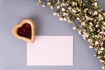 biglietto di auguri con un biscotto a forma di cuore e un mazzo di fiori bianchi