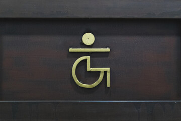 Icono amarillo claro de una persona en silla de ruedas en una puerta de madera de un baño público