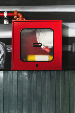 Un extintor y su manguera guardado en una caja roja de cristal en el &aacute;rea de emergencia, debajo una pared de madera