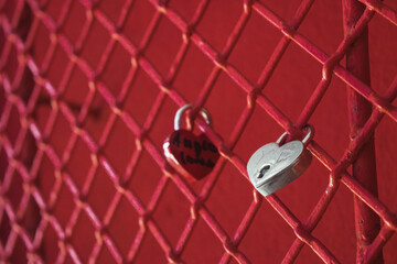 Una reja roja en una pared roja con dos candados cerrados con forma de corazón y algunos desgastes