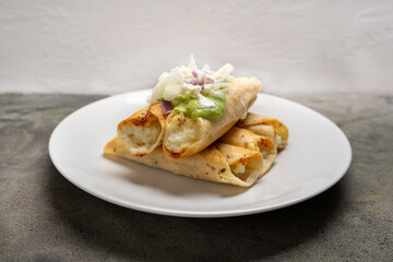 Fried tacos called flautas with guacamole and cabbage on dark background. Mexican food