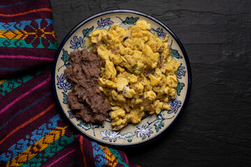 Scrambled eggs with green sauce and refried beans on dark background. Mexican food