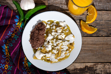 Green chilaquiles with refried beans and cheese on wooden background. Mexican food