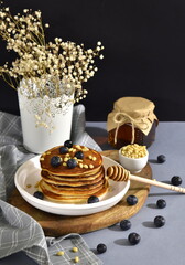 Pancakes with blueberries, pine nuts and honey on a white plate. A jar of honey.