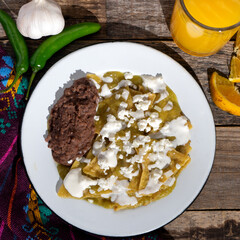 Green chilaquiles with refried beans and cheese on wooden background. Mexican food