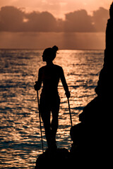 close-up view of silhouette of woman with trekking sticks near cliff against background of sea