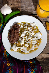 Green chilaquiles with refried beans and cheese on wooden background. Mexican food