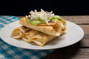 Fried tacos called flautas with guacamole and cabbage on wooden background. Mexican food