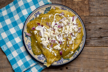 Green enchiladas with fresh cheese and sour cream on wooden background. Mexican food
