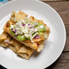 Fried tacos called flautas with guacamole and cabbage on wooden background. Mexican food