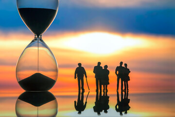 miniature people. silhouettes of different people watching the sunset next to the hourglass. end of...