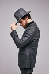 Side View Portrait of Young Male In Suit Posing Looking Down, Touching Hat. Young Confident Guy Alone Posing In Studio