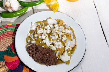 Green chilaquiles with refried beans and cheese on white background. Mexican food