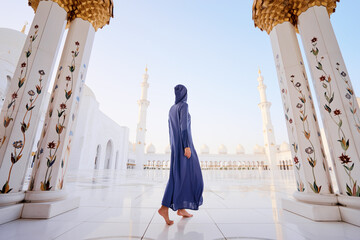 Traveling by Unated Arabic Emirates. Woman in traditional abaya standing in the Sheikh Zayed Grand Mosque, famous Abu Dhabi sightseeing. - obrazy, fototapety, plakaty